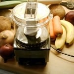 food processor surrounded by carrots and bananas