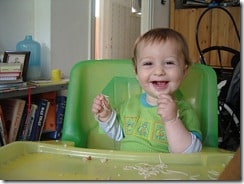 baby in a green highchair eating spaghetti