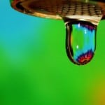 A drop of water from a faucet on a green/blue background