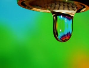 A drop of water from a faucet on a green/blue background